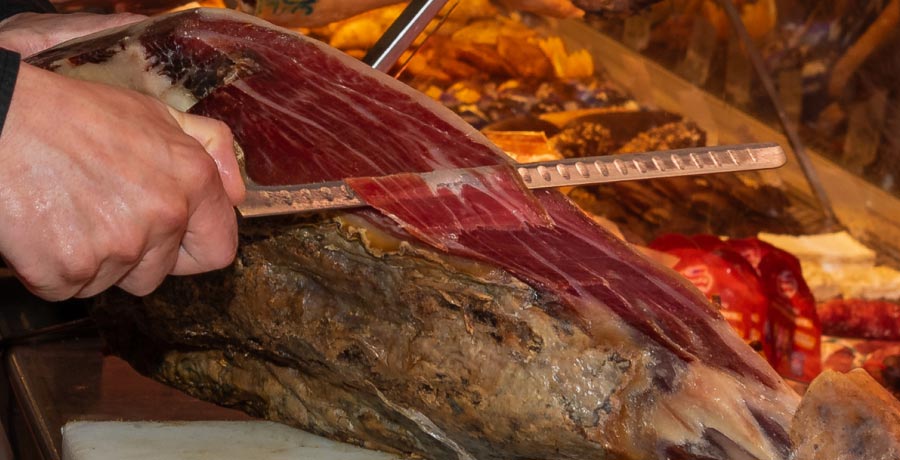 Corte de jamón ibérico con cuchillo profesional, mostrando su veteado y textura.