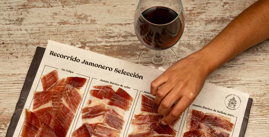 Selección de jamón ibérico acompañada de una copa de vino tinto sobre una mesa.