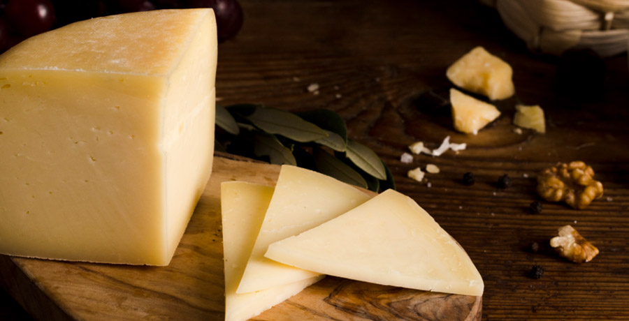 Queso de oveja curado cortado en cuñas sobre tabla de madera con nueces y laurel