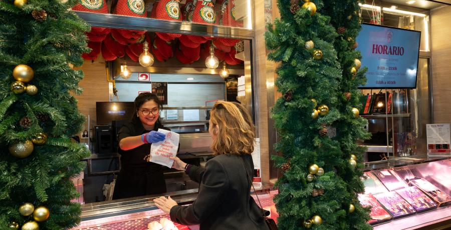 Mercadillos Navidad Madrid 2025: cliente recogiendo bolsa en mostrador del Museo del Jamón decorado con guirnaldas